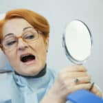 woman in dental chair looking at teeth in mirror