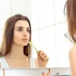 young woman brushes her teeth in the mirror